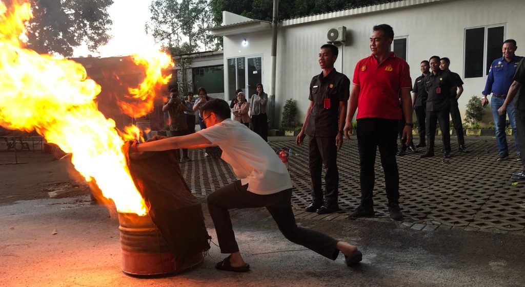 Client staff practicing fire safety by using a fire blanket to cover a controlled burning drum during a training exercise