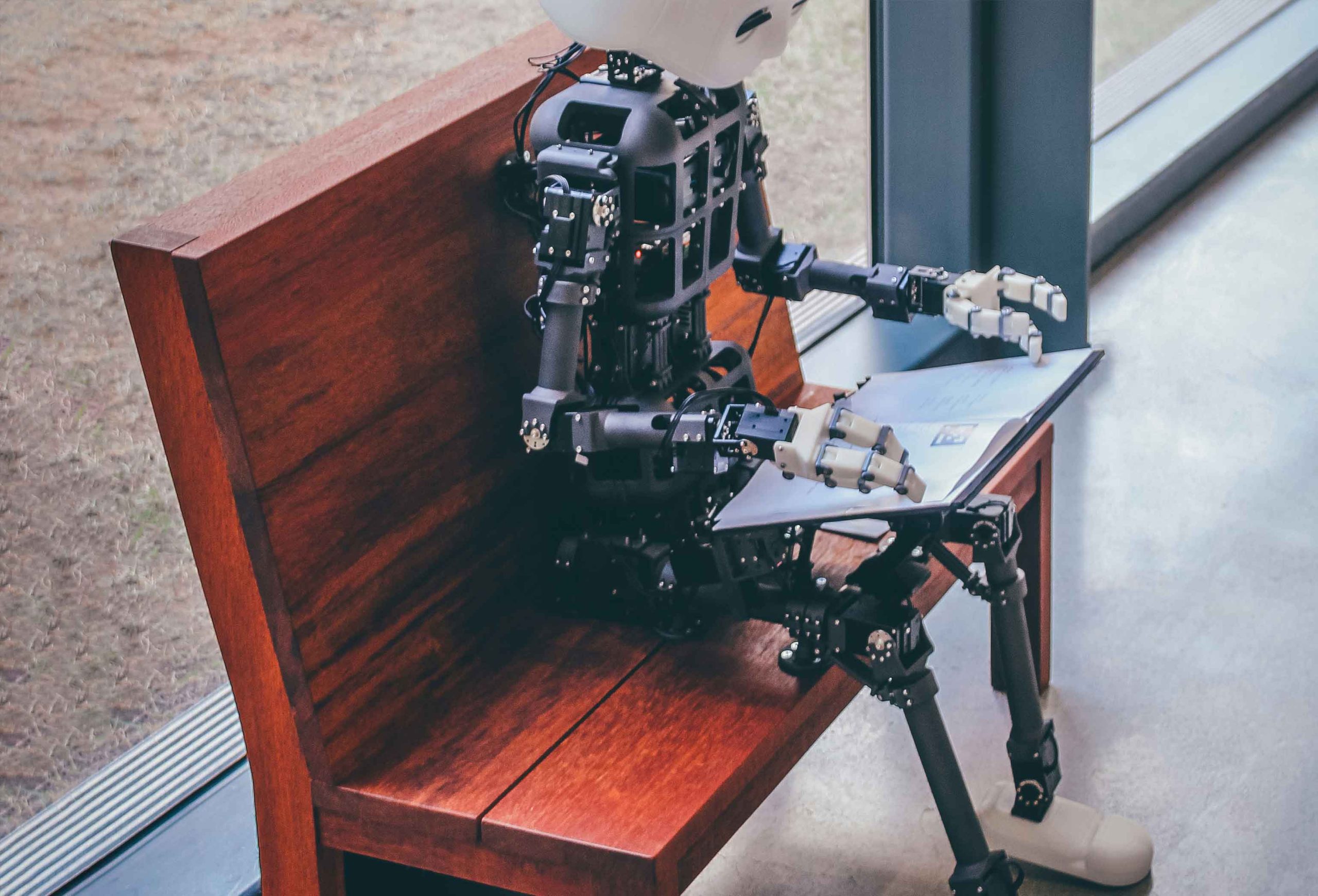 Robot seated on a bench indoor reading a book